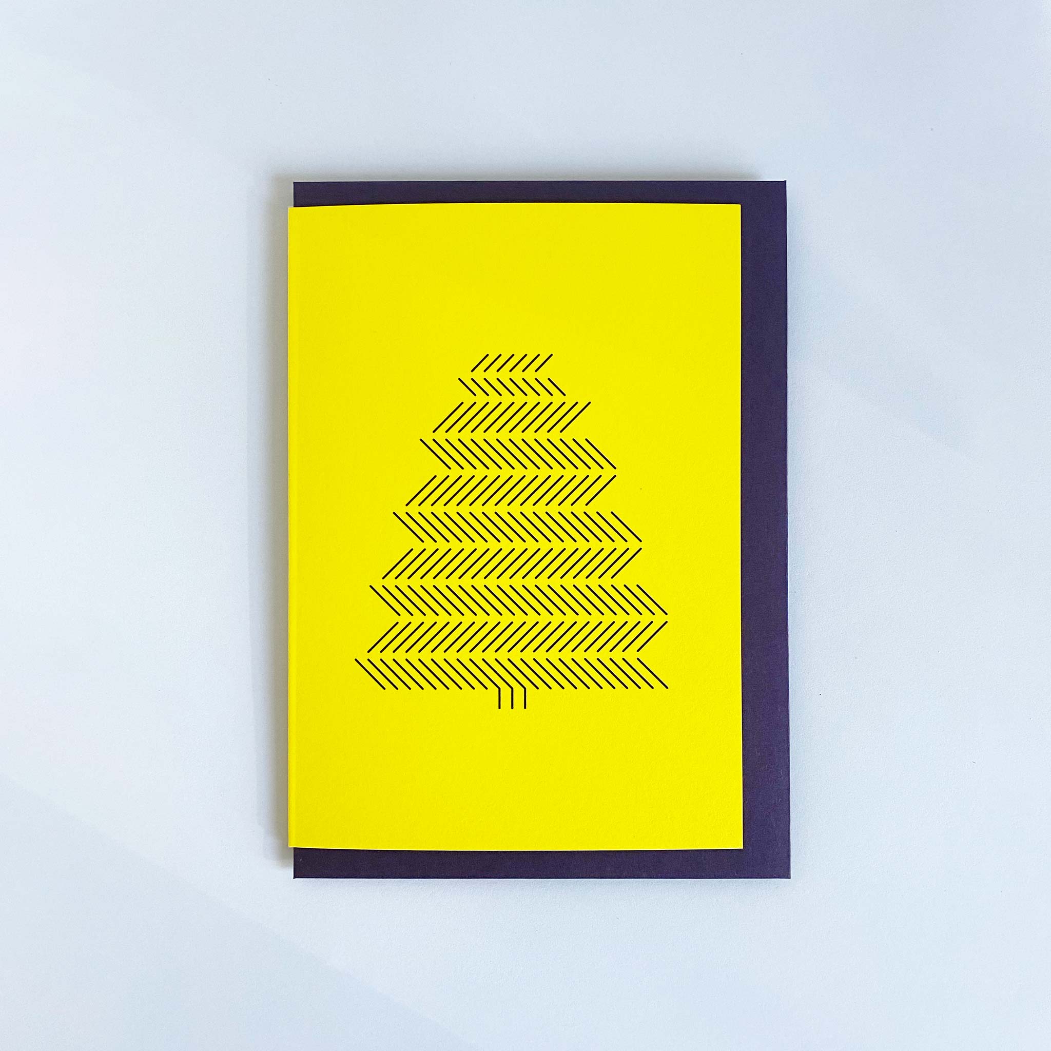 Yellow A6 christmas greeting card with black print of pine tree and purple envelope