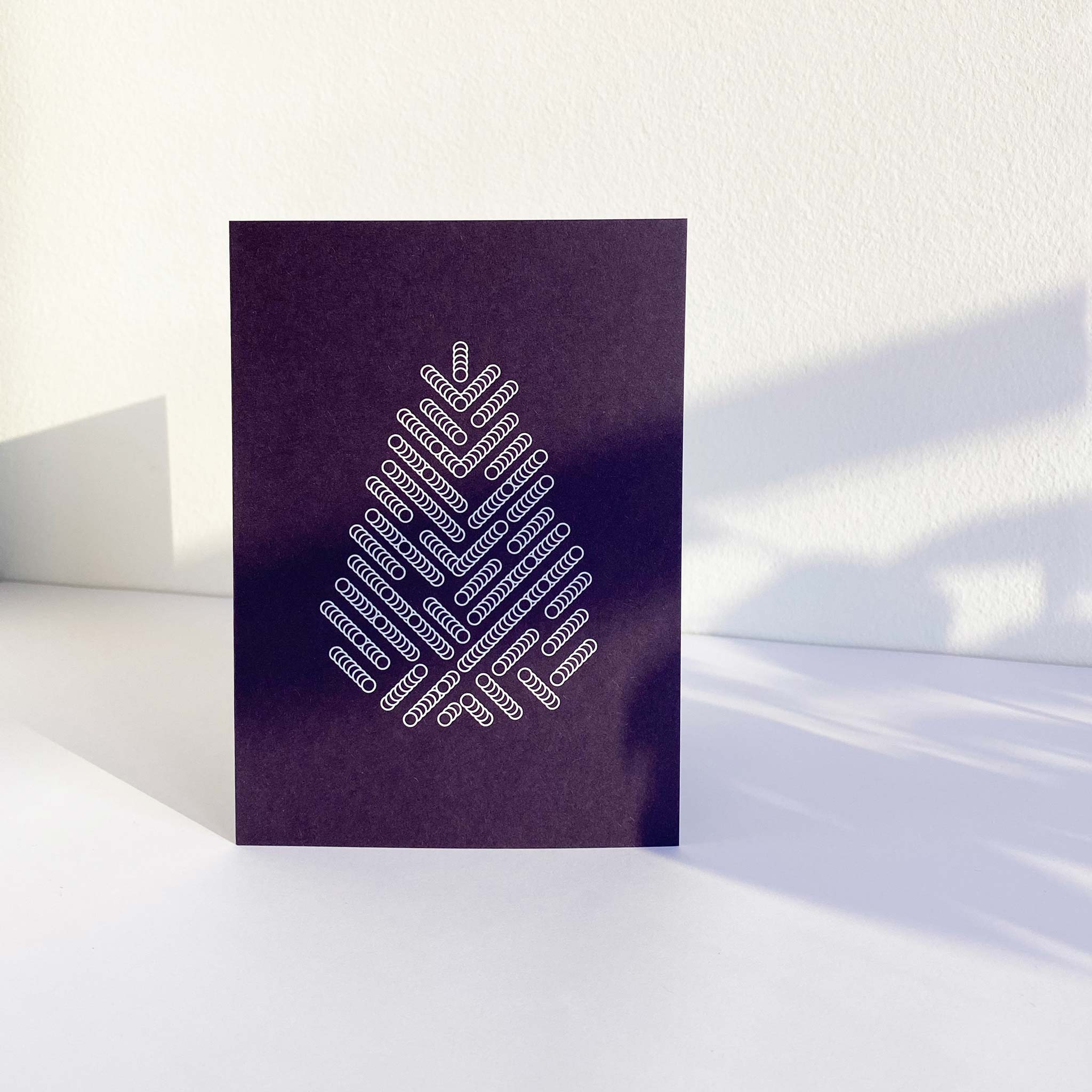 Standing deep purple A6 christmas greeting card printed with white graphic print of spruce tree.